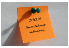 Ein orangefarbener Klebezettel mit schwarzer Schrift, "29.10.2025 Veranstaltungs-ankündigung", ist mit einer grünen Reißzwecke an einer weißen Wand befestigt.